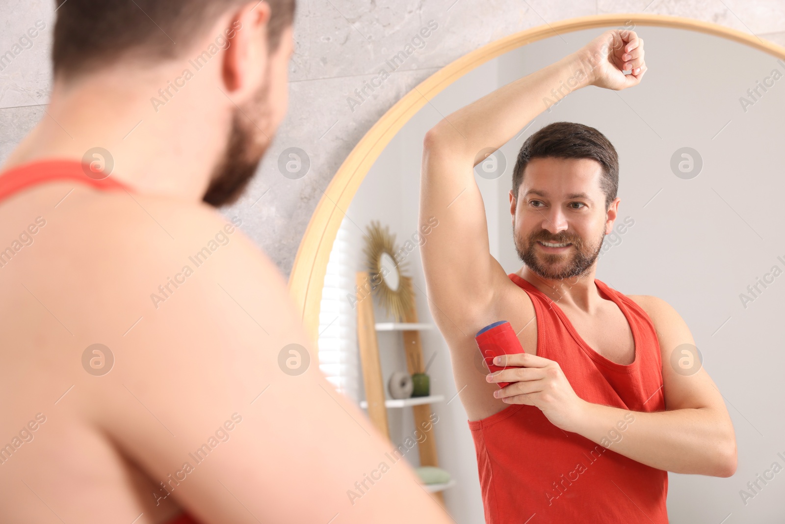 Photo of Smiling man applying solid deodorant near mirror at home