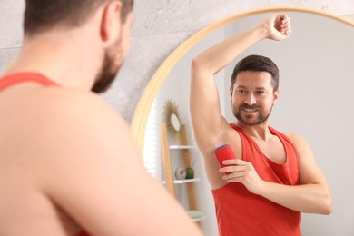 Smiling man applying solid deodorant near mirror at home