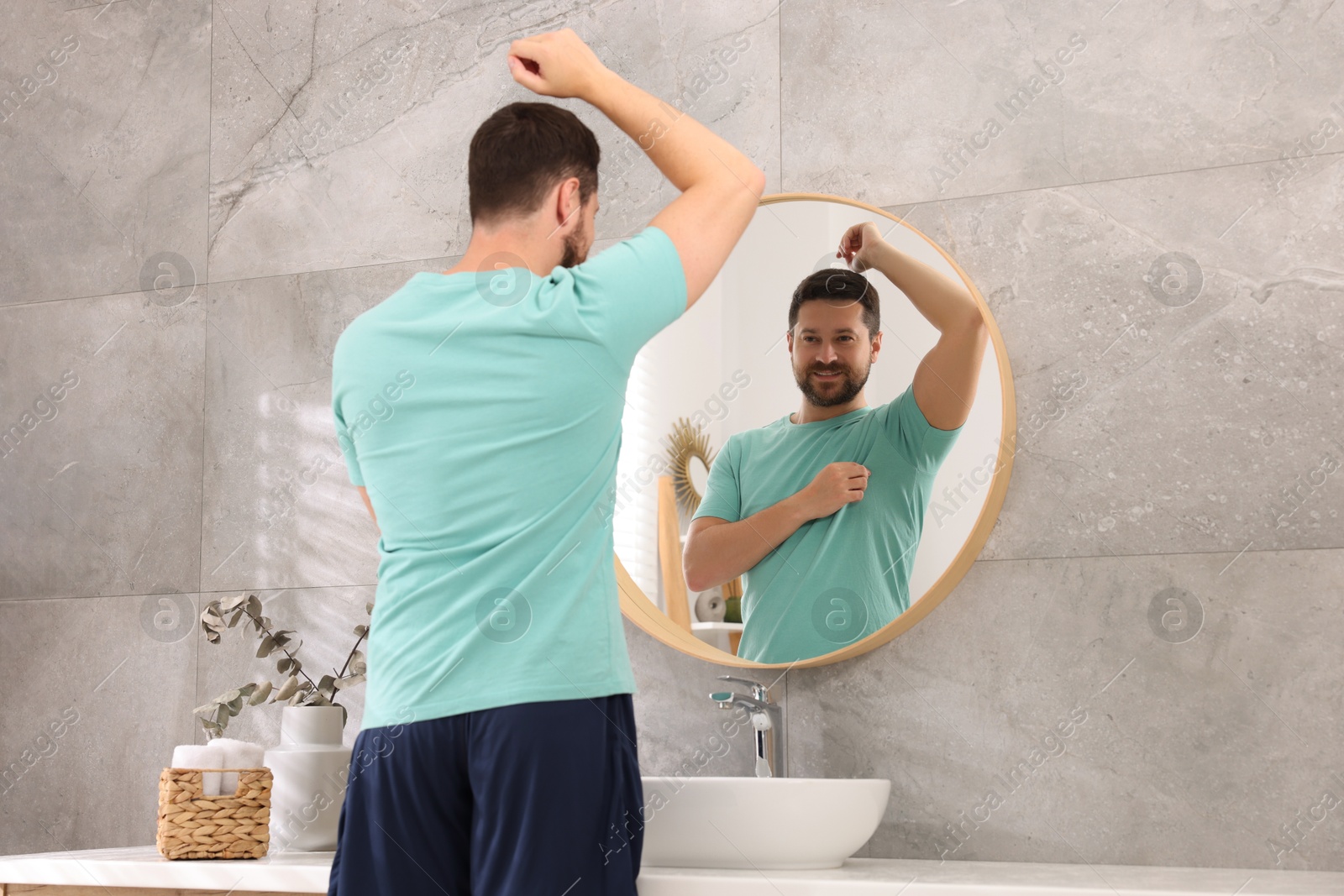 Photo of Smiling man after using deodorant near mirror at home, back view