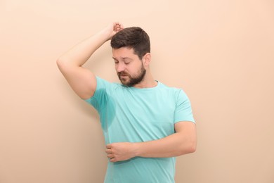 Emotional man in t-shirt before using deodorant on beige background