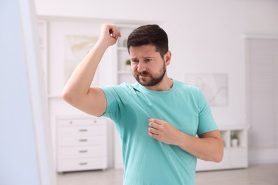 Photo of Emotional man in t-shirt before using deodorant at home