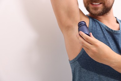 Photo of Smiling man applying roll-on deodorant on white background, closeup. Space for text