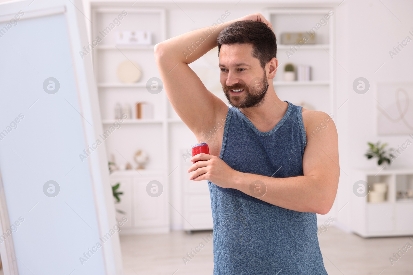 Photo of Smiling man applying solid deodorant at home