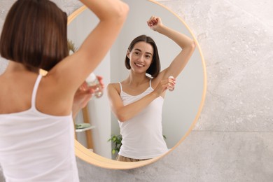 Photo of Smiling woman applying roll-on deodorant near mirror at home