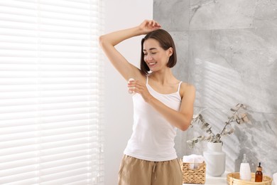 Photo of Smiling woman applying roll-on deodorant at home