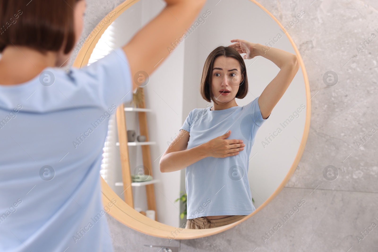 Photo of Emotional woman in t-shirt before using deodorant near mirror at home