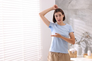 Photo of Emotional woman in t-shirt before using deodorant at home. Space for text