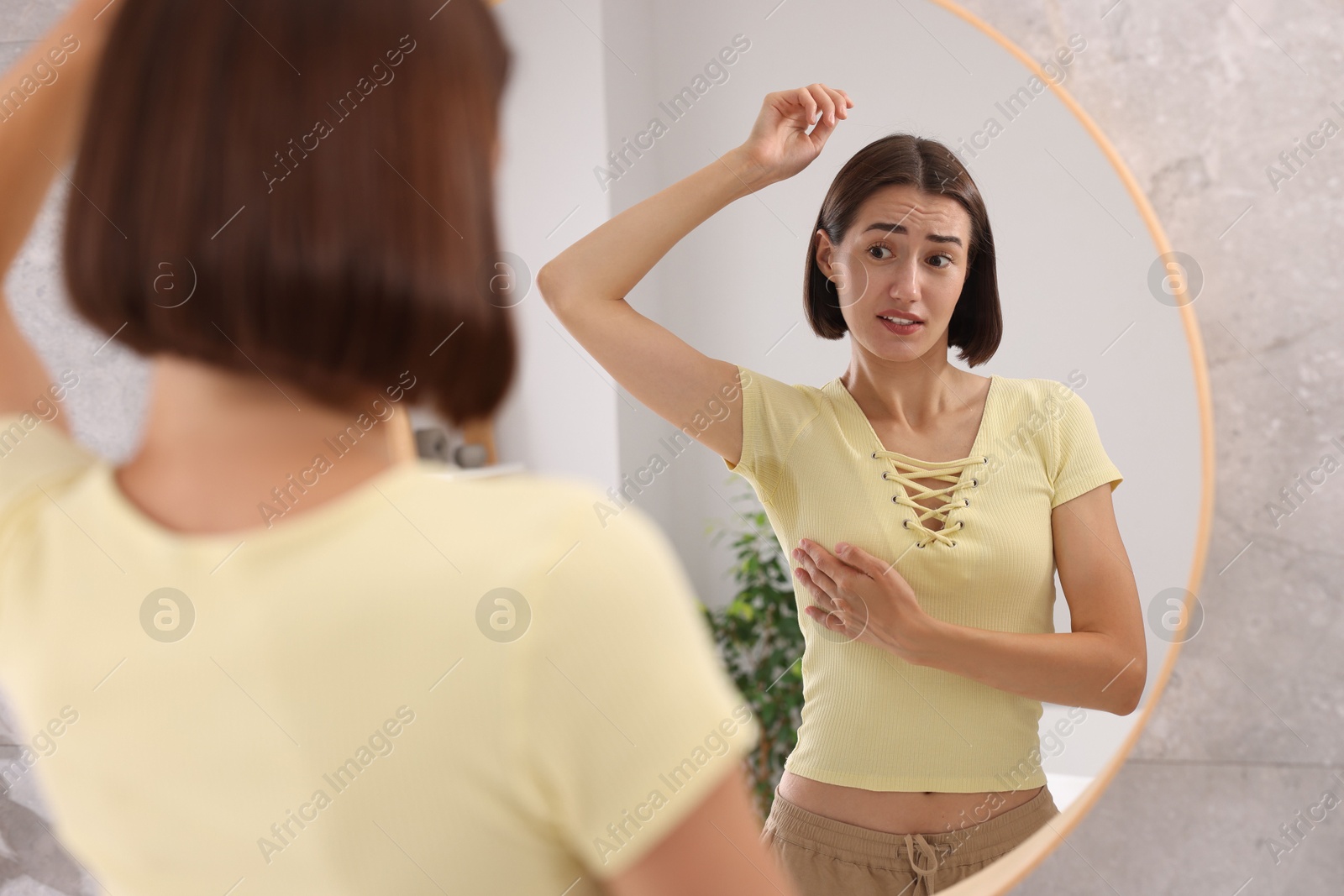 Photo of Emotional woman in t-shirt before using deodorant near mirror at home