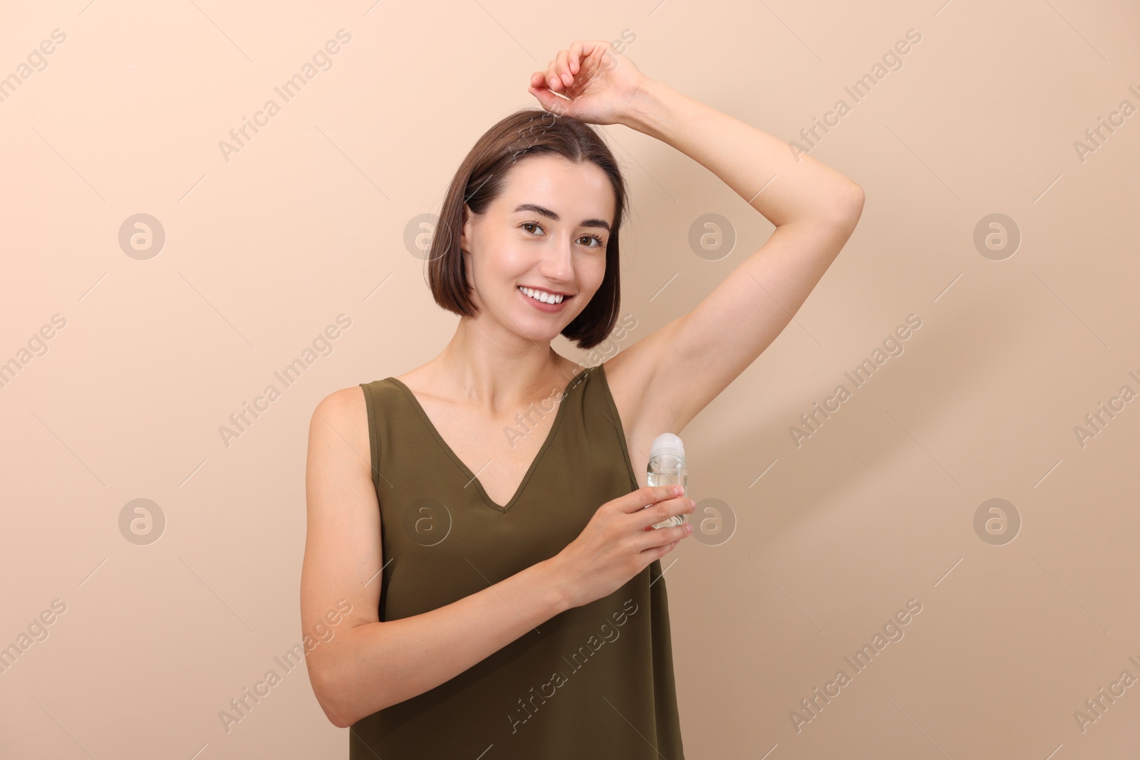 Photo of Smiling woman applying roll-on deodorant on beige background