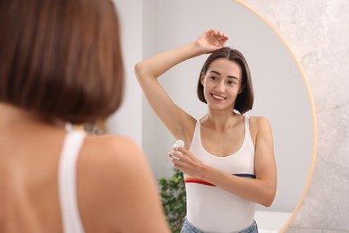 Photo of Smiling woman applying roll-on deodorant near mirror at home