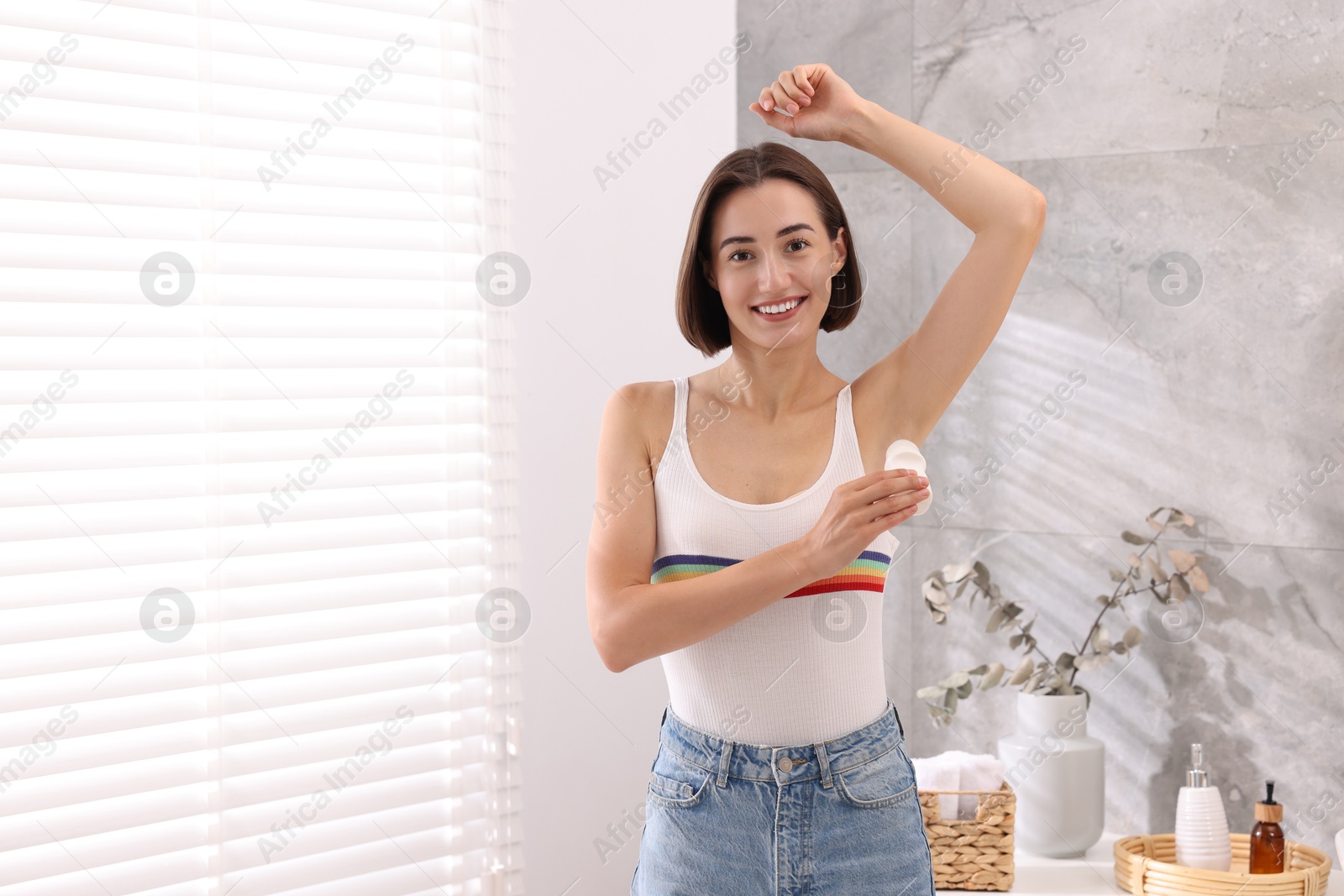 Photo of Smiling woman applying roll-on deodorant at home. Space for text