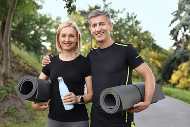 Photo of Happy couple with bottle of water and fitness mats in park