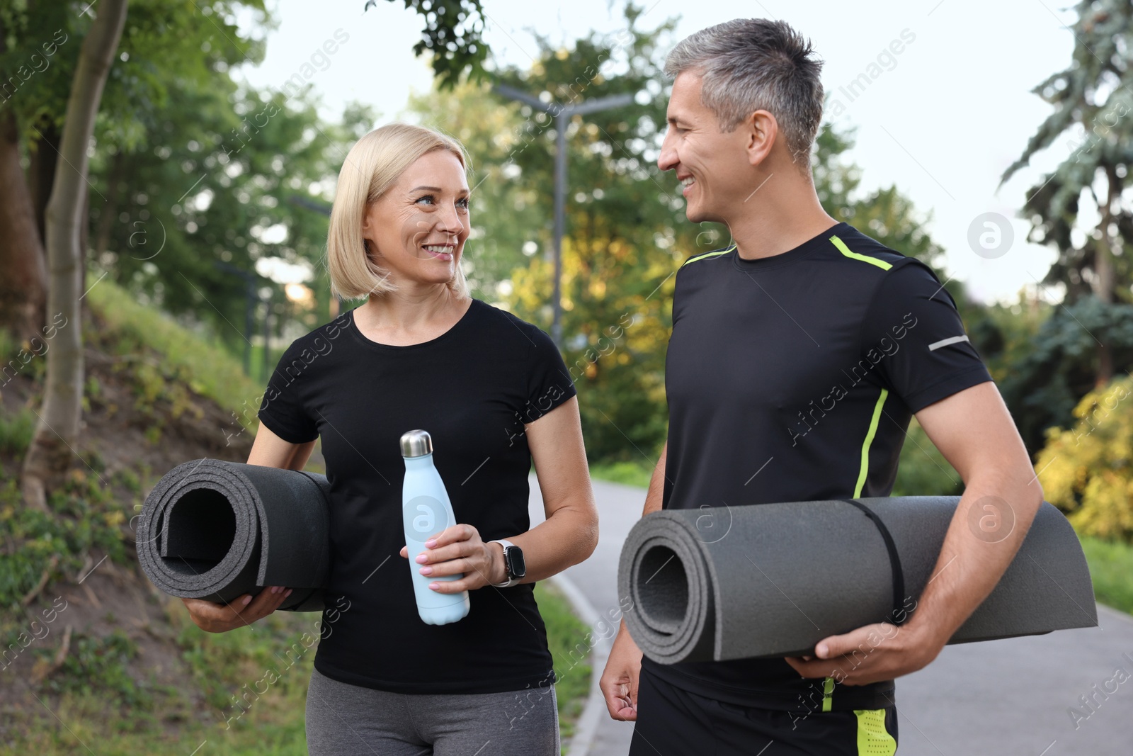 Photo of Happy couple with bottle of water and fitness mats in park