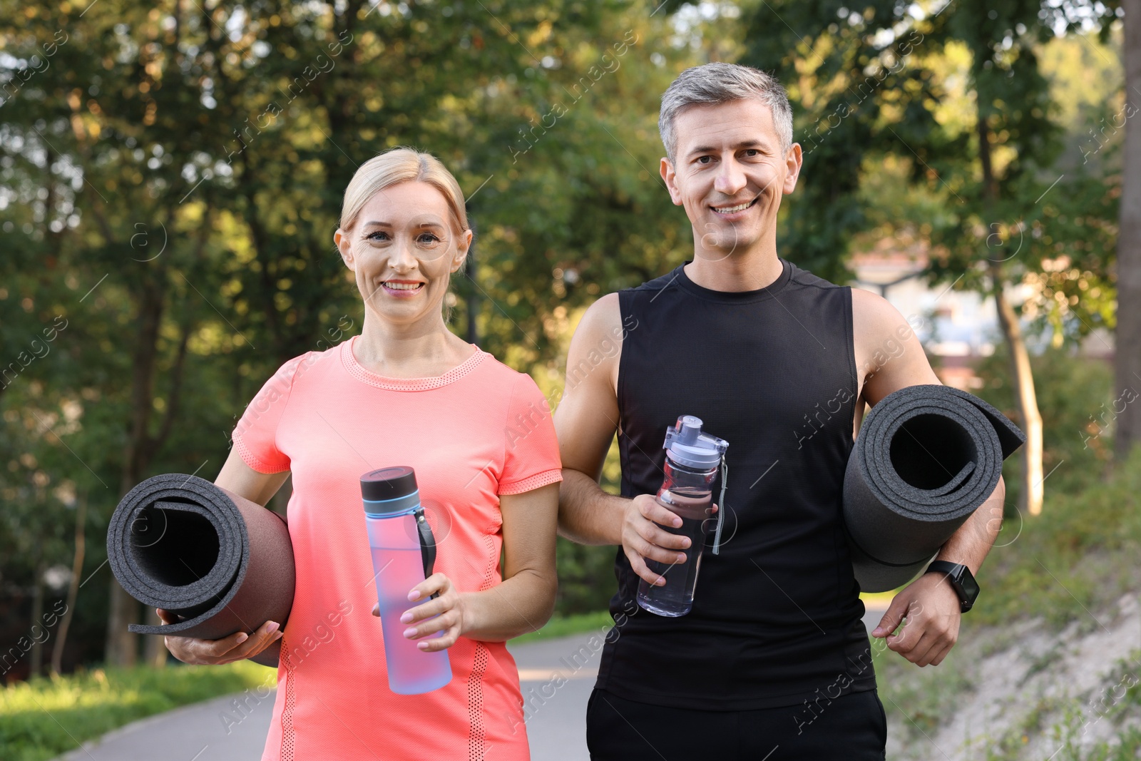 Photo of Happy couple with bottles of water and fitness mats in park