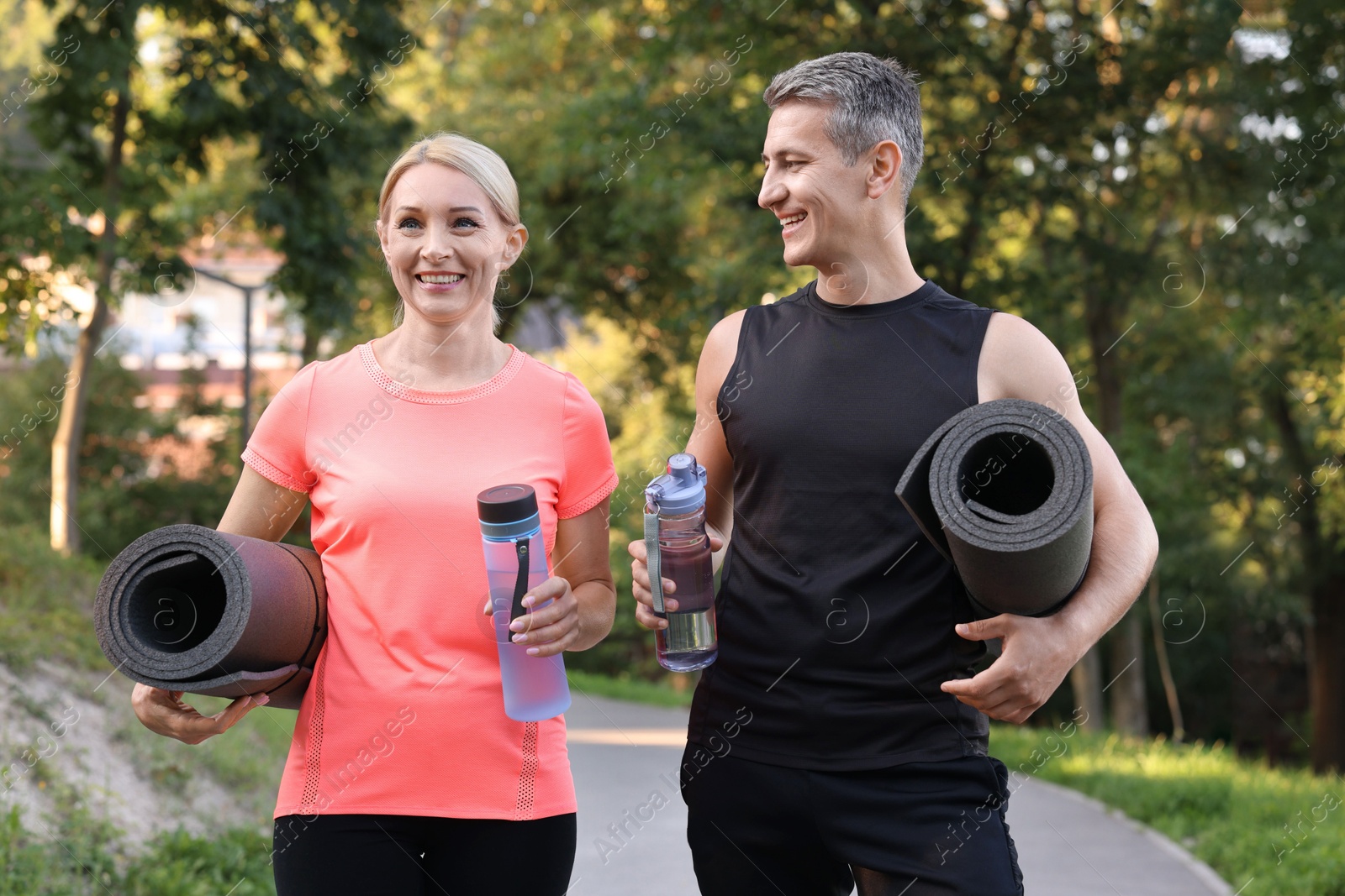 Photo of Happy couple with bottles of water and fitness mats in park