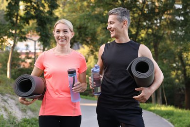 Photo of Happy couple with bottles of water and fitness mats in park