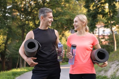 Photo of Happy couple with bottles of water and fitness mats in park