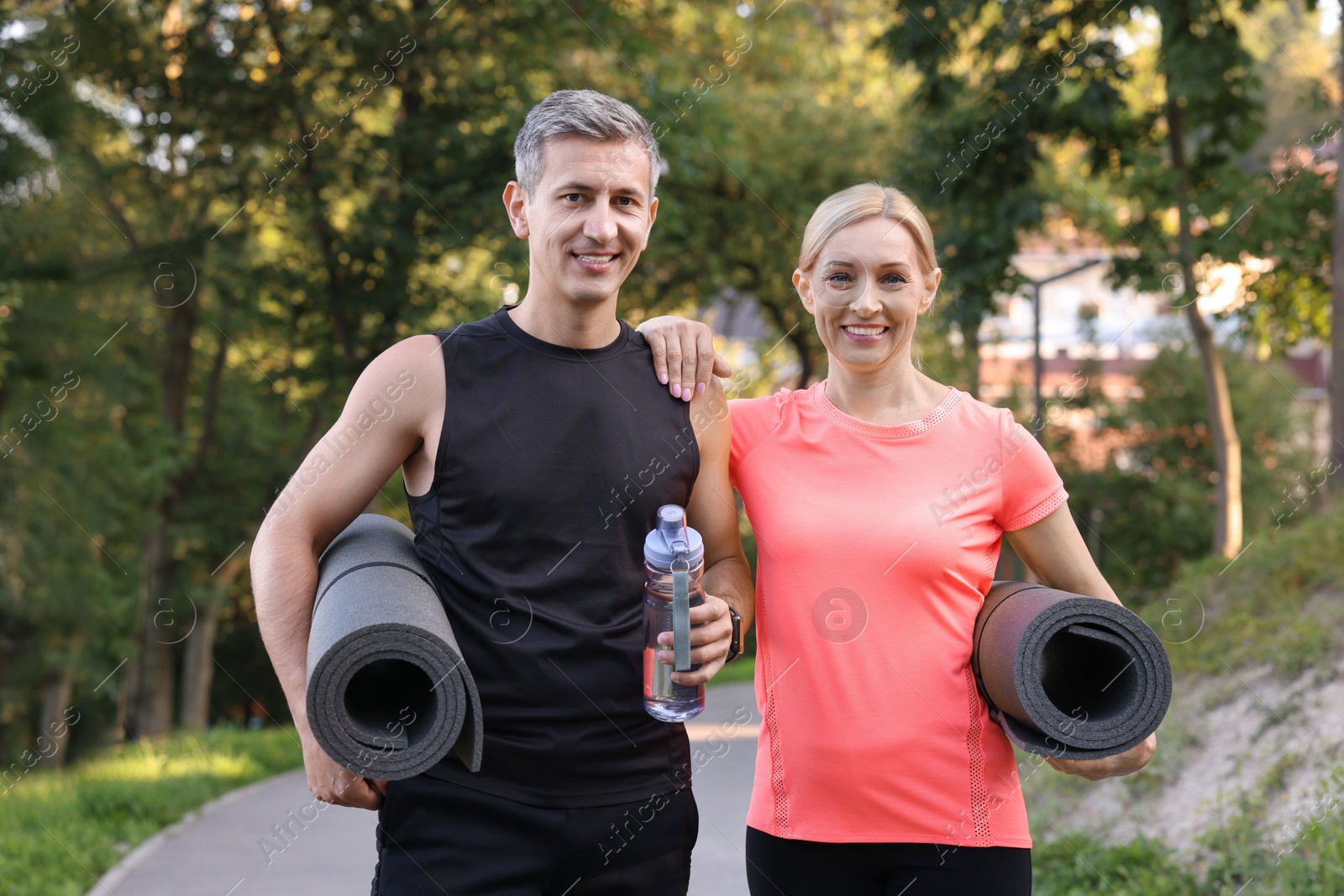 Photo of Happy couple with bottle of water and fitness mats in park