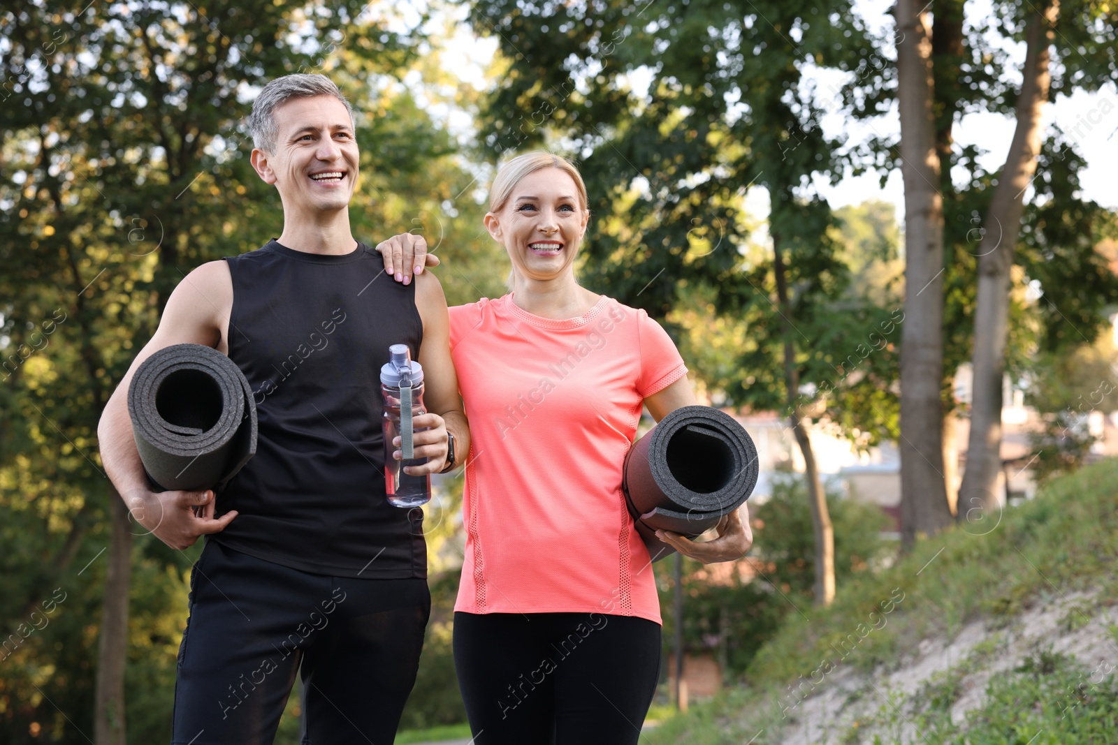 Photo of Happy couple with bottle of water and fitness mats in park