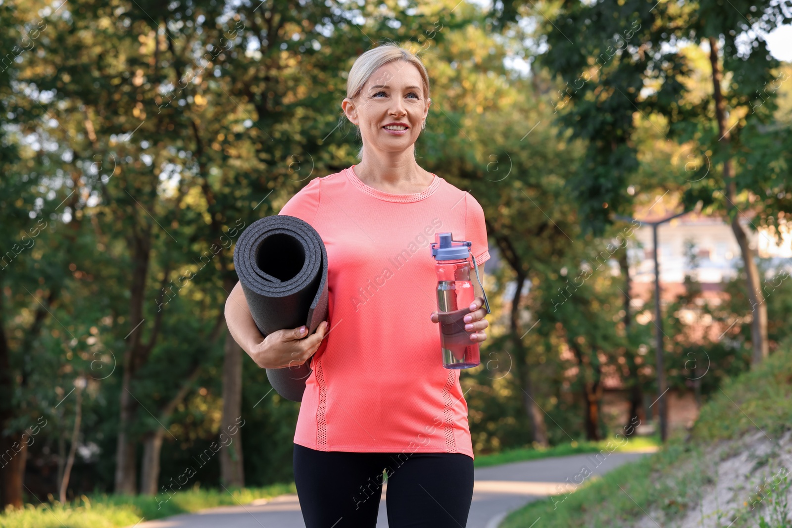 Photo of Happy woman with bottle of water and fitness mat in park