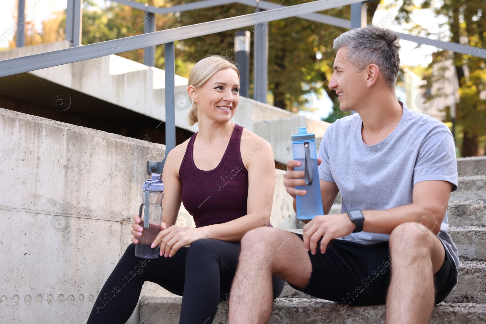 Photo of Smiling couple with bottles of water on steps outdoors