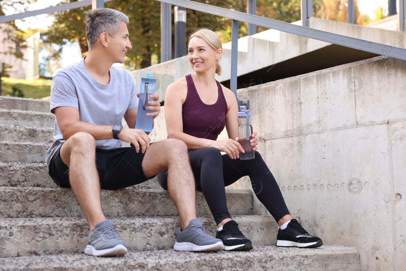 Photo of Smiling couple with bottles of water on steps outdoors