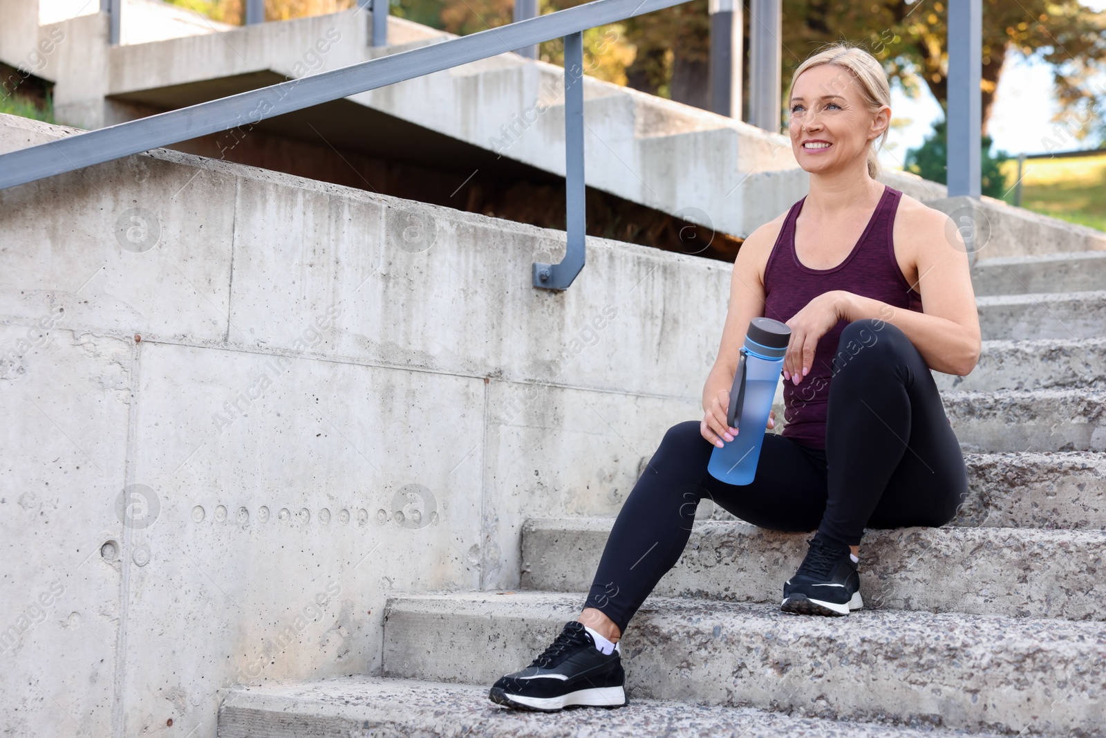 Photo of Smiling woman with bottle of water on steps outdoors