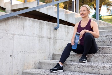 Photo of Smiling woman with bottle of water on steps outdoors