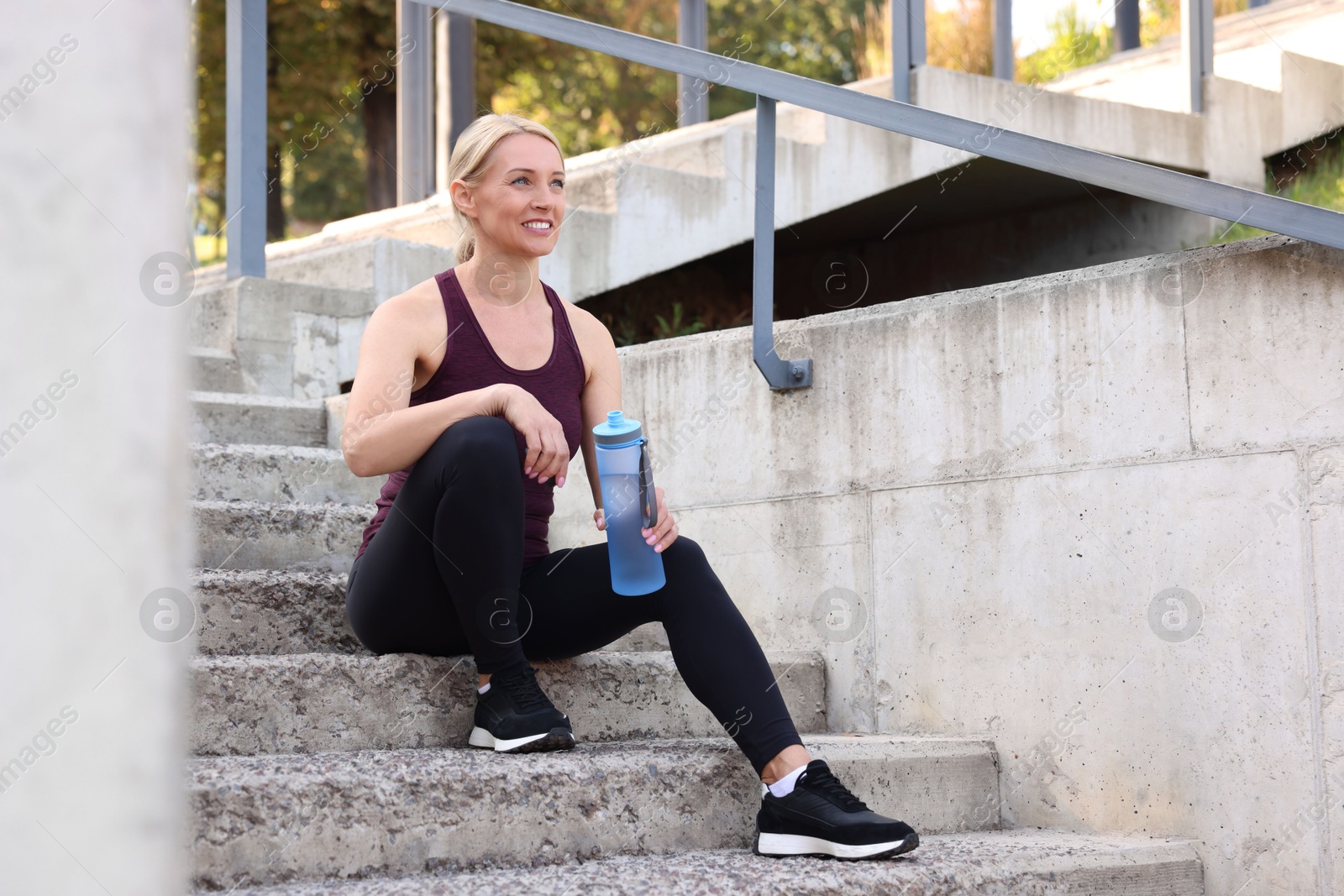 Photo of Smiling woman with bottle of water on steps outdoors