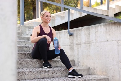 Photo of Smiling woman with bottle of water on steps outdoors