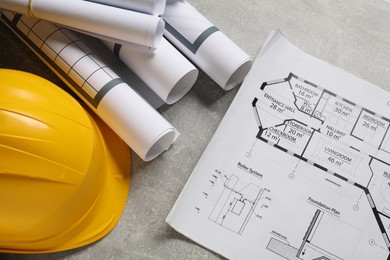 Photo of Different engineering drawings and hard hat on grey textured table, flat lay