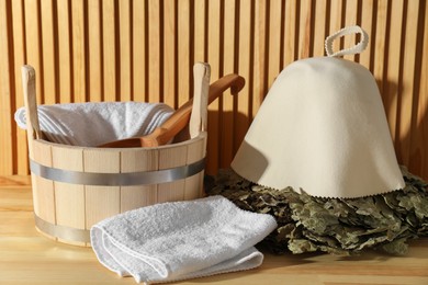 Photo of Oak sauna whisk, felt wool hat, towels, bucket and ladle on wooden surface