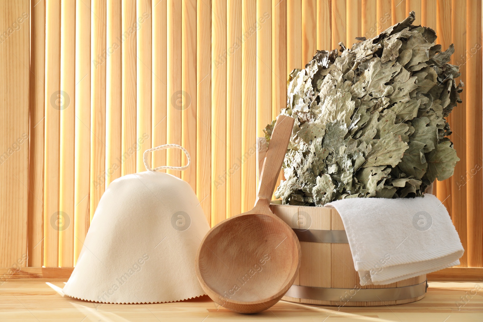 Photo of Sauna equipment. Bucket, ladle, towel and oak whisk on wooden surface