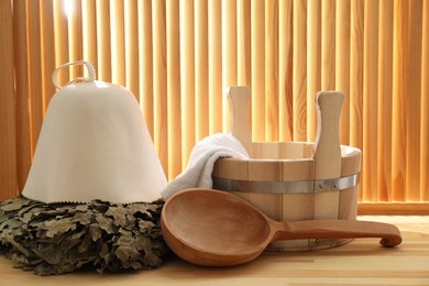 Sauna equipment. Bucket, ladle, towel, oak whisk and felt wool hat on wooden surface