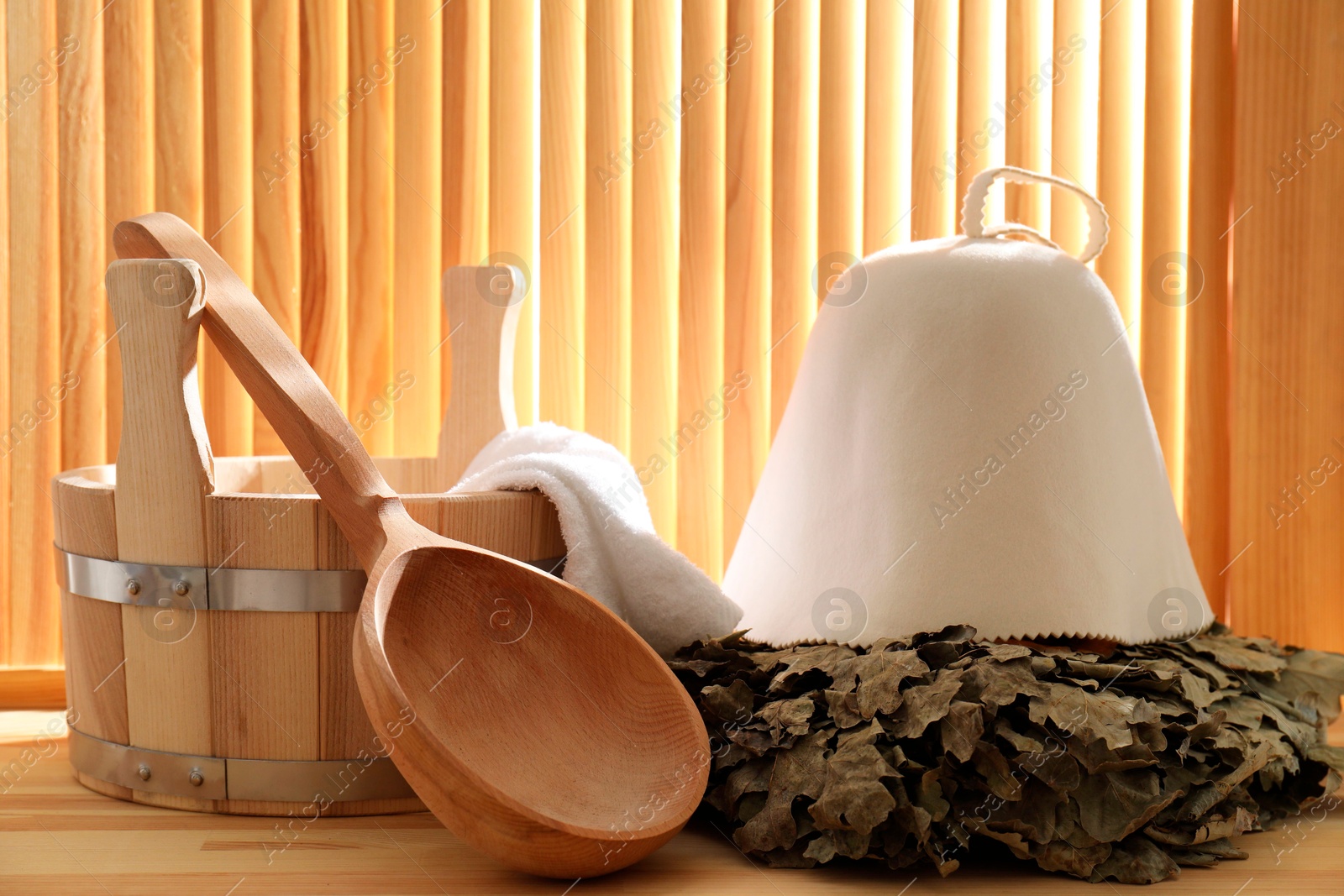 Photo of Sauna equipment. Bucket, ladle, towel, oak whisk and felt wool hat on wooden surface