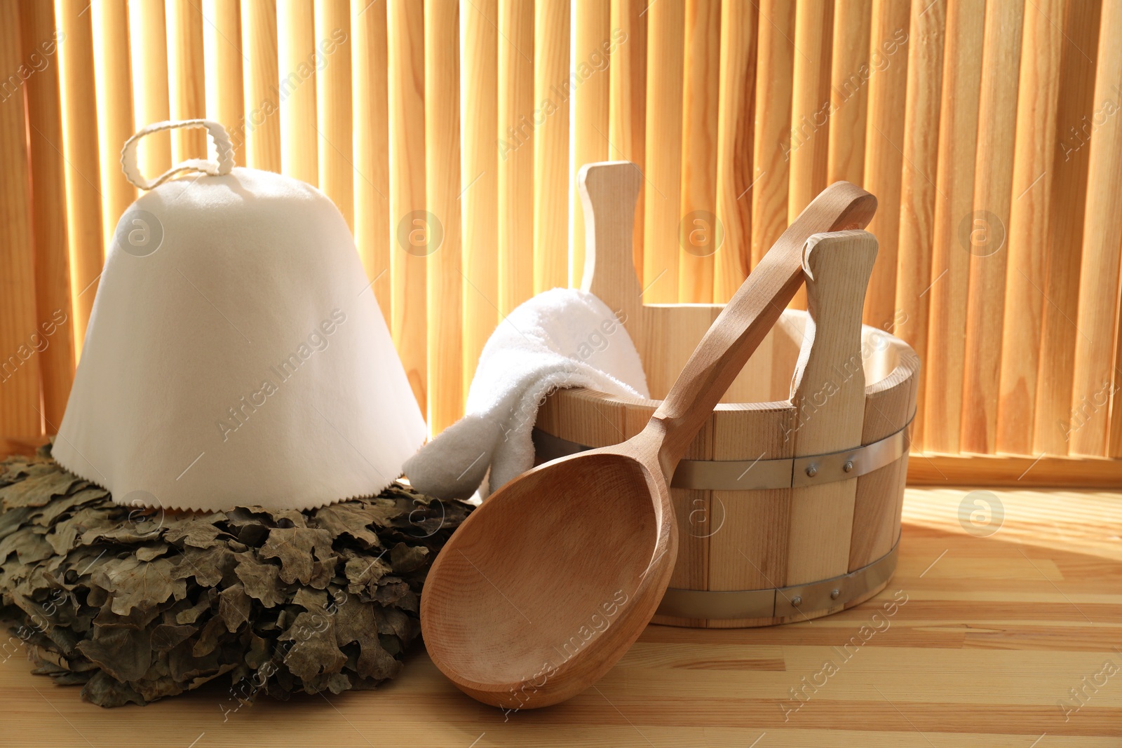 Photo of Sauna equipment. Bucket, ladle, towel, oak whisk and felt wool hat on wooden surface