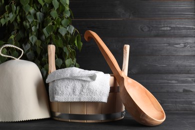 Photo of Sauna equipment. Felt wool hat, wooden bucket, towel and ladle on black table