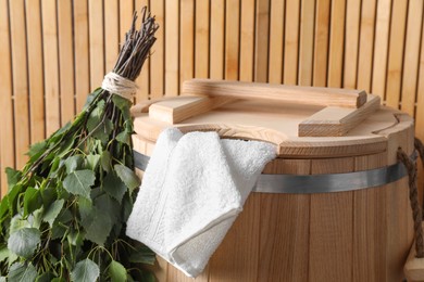 Photo of Sauna equipment. Bucket, towel and oak whisk against wooden wall