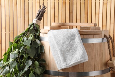 Photo of Sauna equipment. Bucket, towel and oak whisk against wooden wall