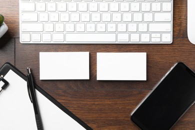 Photo of Blank business cards, clipboard with sheet, smartphone, keyboard and pen on wooden table, flat lay. Mockup for design