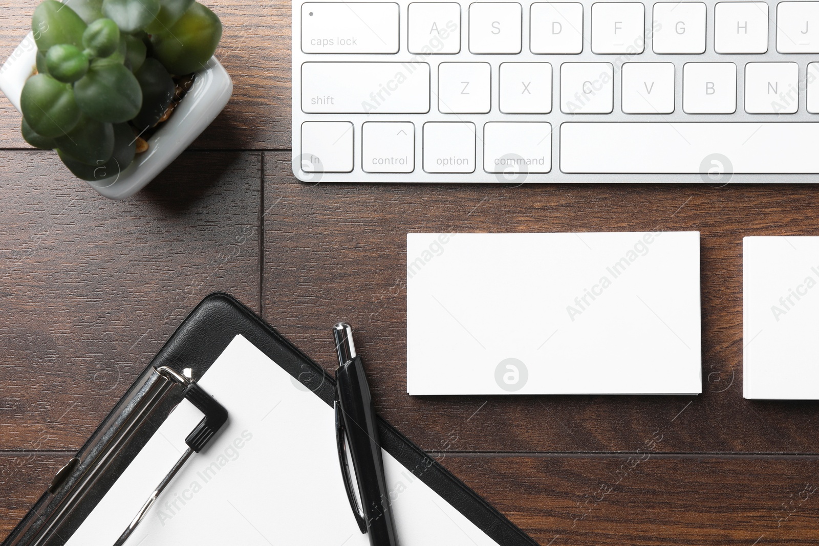 Photo of Blank business cards, clipboard with sheet, keyboard and pen on wooden table, flat lay. Mockup for design