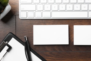 Photo of Blank business cards, clipboard with sheet, keyboard and pen on wooden table, flat lay. Mockup for design