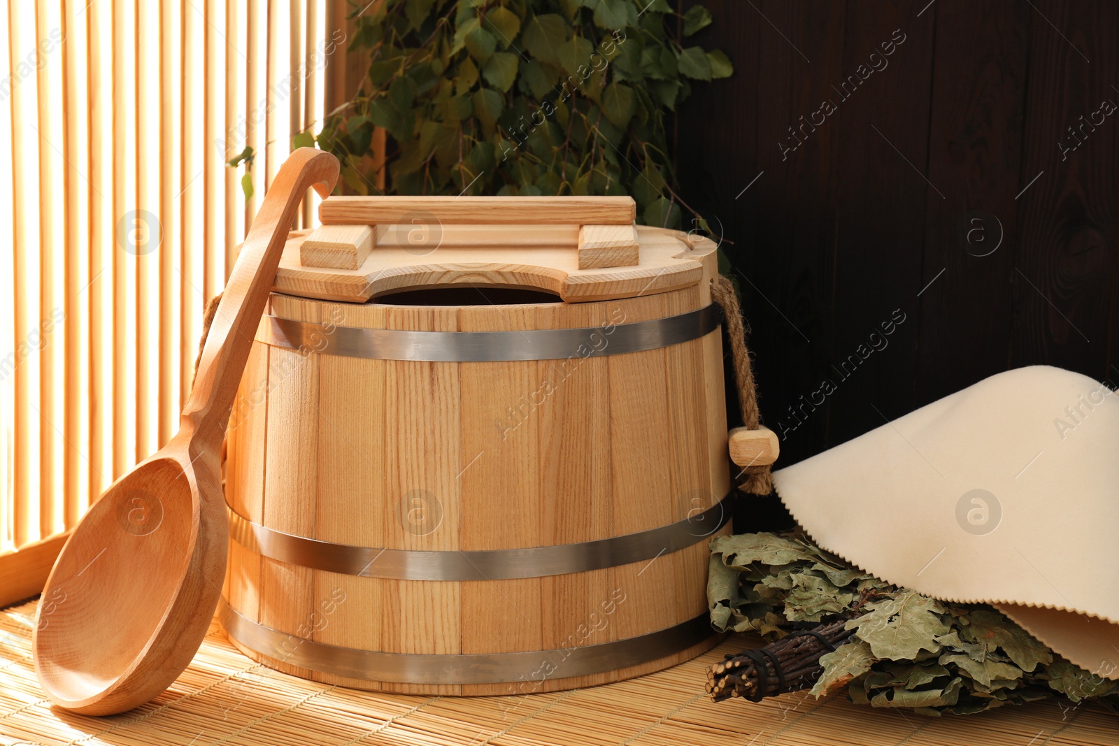 Photo of Sauna equipment. Bucket, ladle, felt wool hat and whisks on bamboo bench indoors