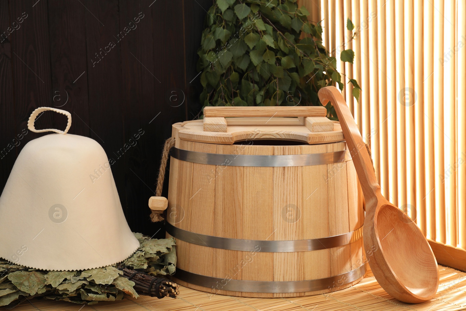 Photo of Sauna equipment. Bucket, ladle, felt wool hat and whisks on bamboo bench indoors