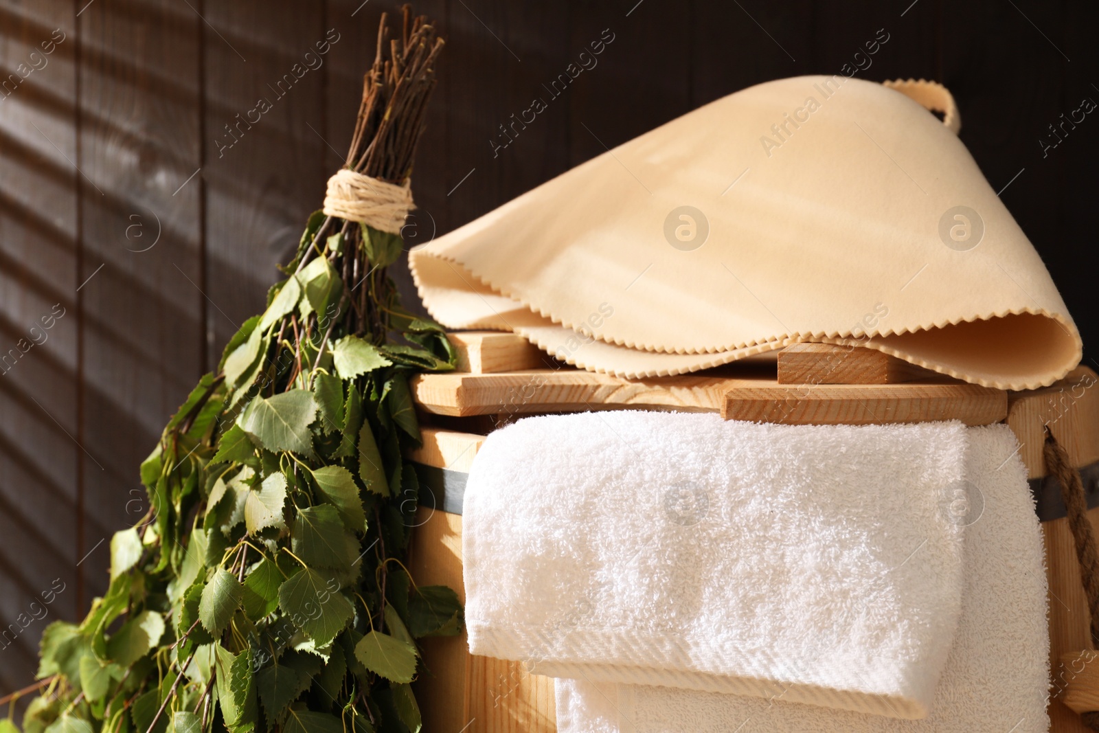 Photo of Sauna equipment. Bucket, felt wool hat, birch whisk and towel on against wooden wall, closeup