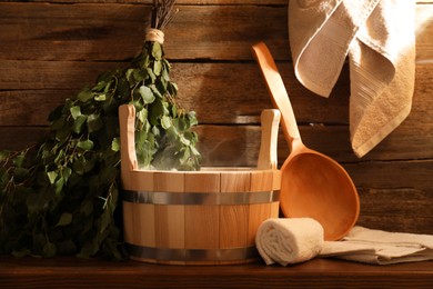 Photo of Sauna equipment. Bucket, ladle, birch whisk and towels on wooden table indoors