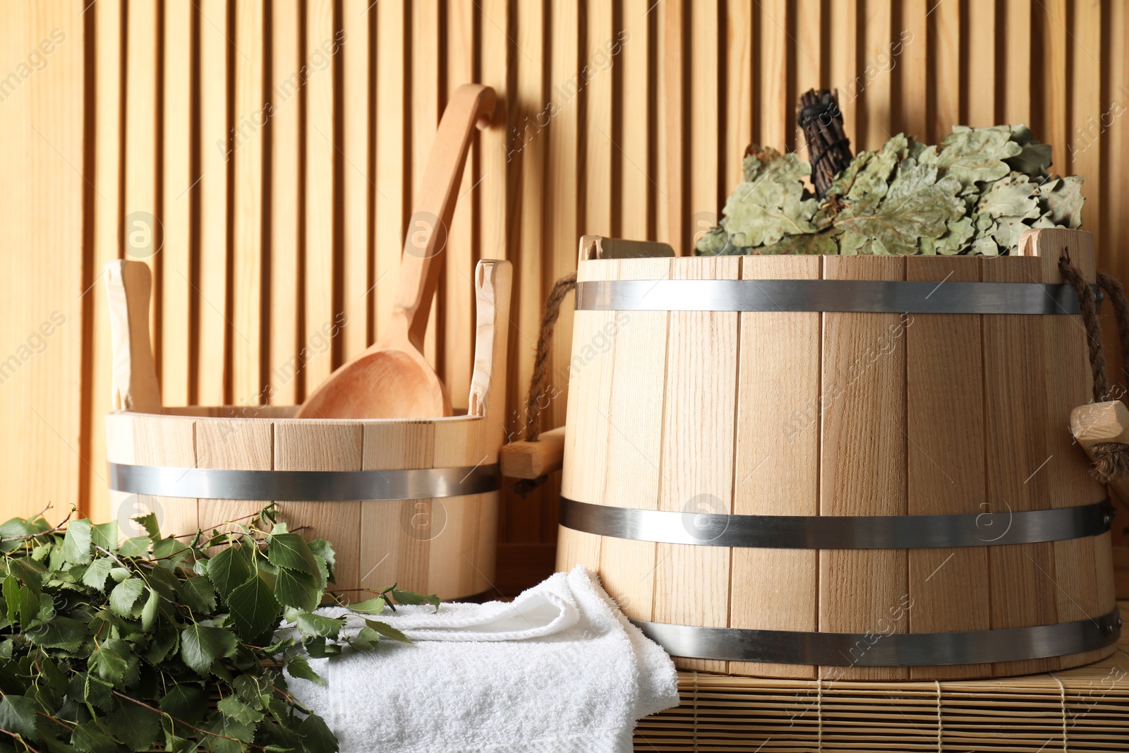 Photo of Sauna equipment. Buckets, whisks, ladle, and towel on bamboo bench near wooden wall