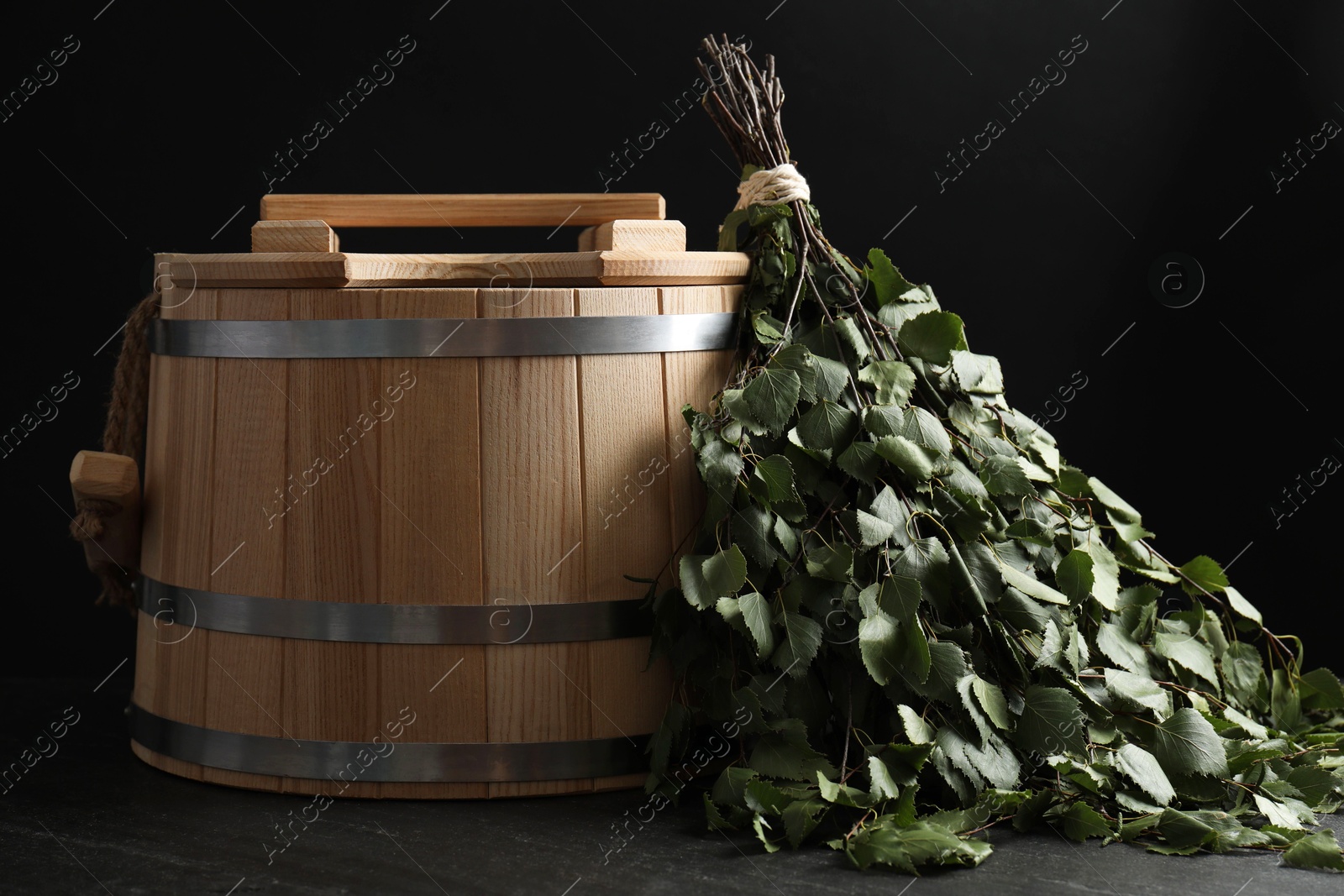 Photo of Sauna equipment. Bucket and birch whisk on black textured surface