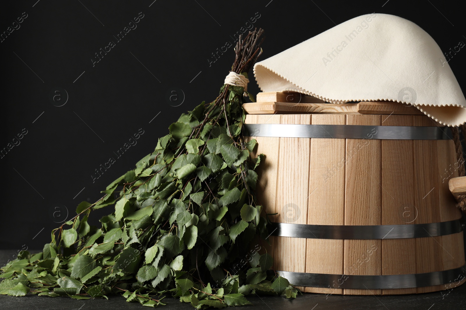 Photo of Sauna equipment. Bucket, birch whisk and felt wool hat on black textured surface