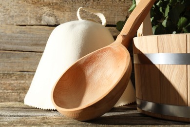 Photo of Sauna equipment. Bucket, felt wool hat and ladle on wooden surface, closeup